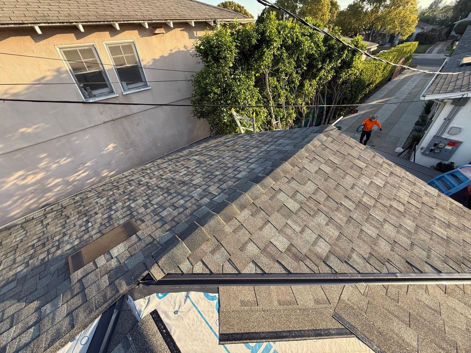 Roofer in orange safety gear walks completed asphalt shingle roof slope in Southern California