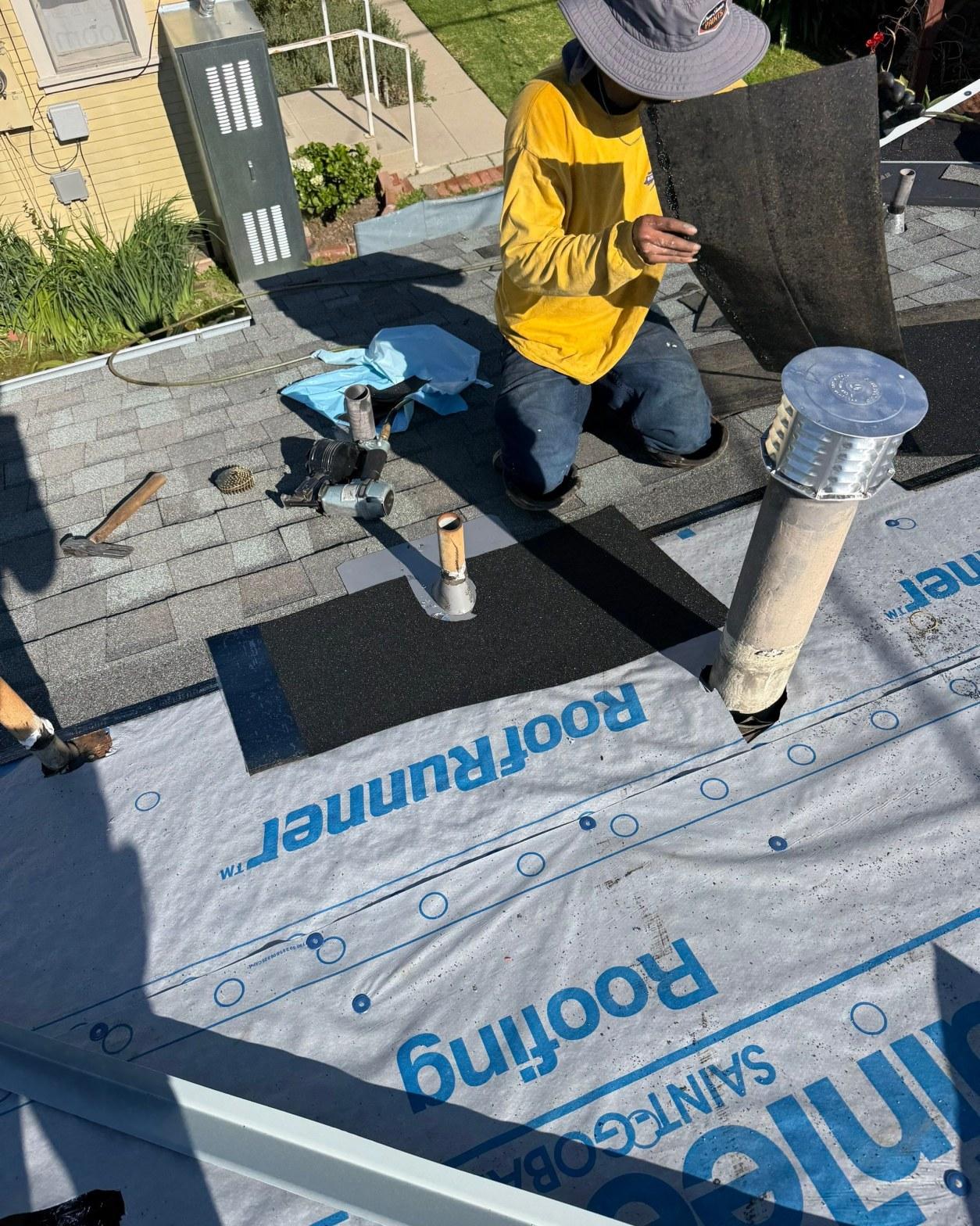 Roofer kneeling on roof laying asphalt shingles over Saint-Gobain RoofRunner underlayment with plumbing pipe boots.