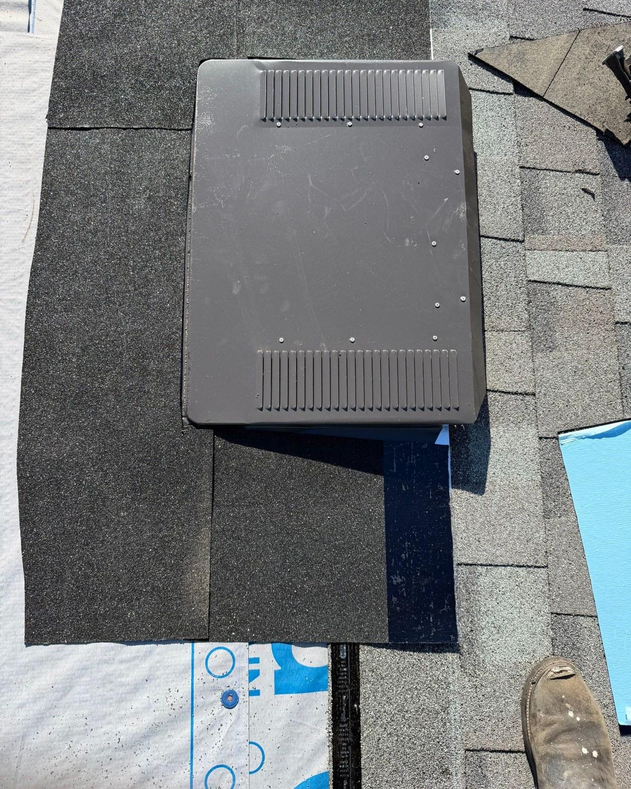Dark gray square roof exhaust vent installed on new asphalt shingles with underlayment visible below.
