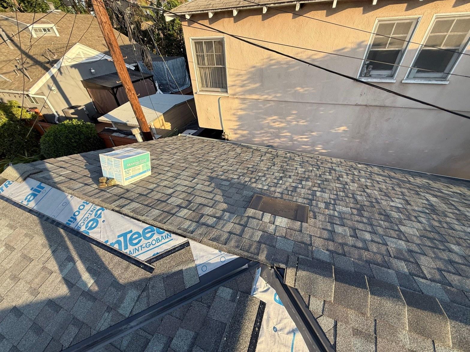Freshly installed gray asphalt shingles on residential roof with CertainTeed ridge cap box and underlayment visible.