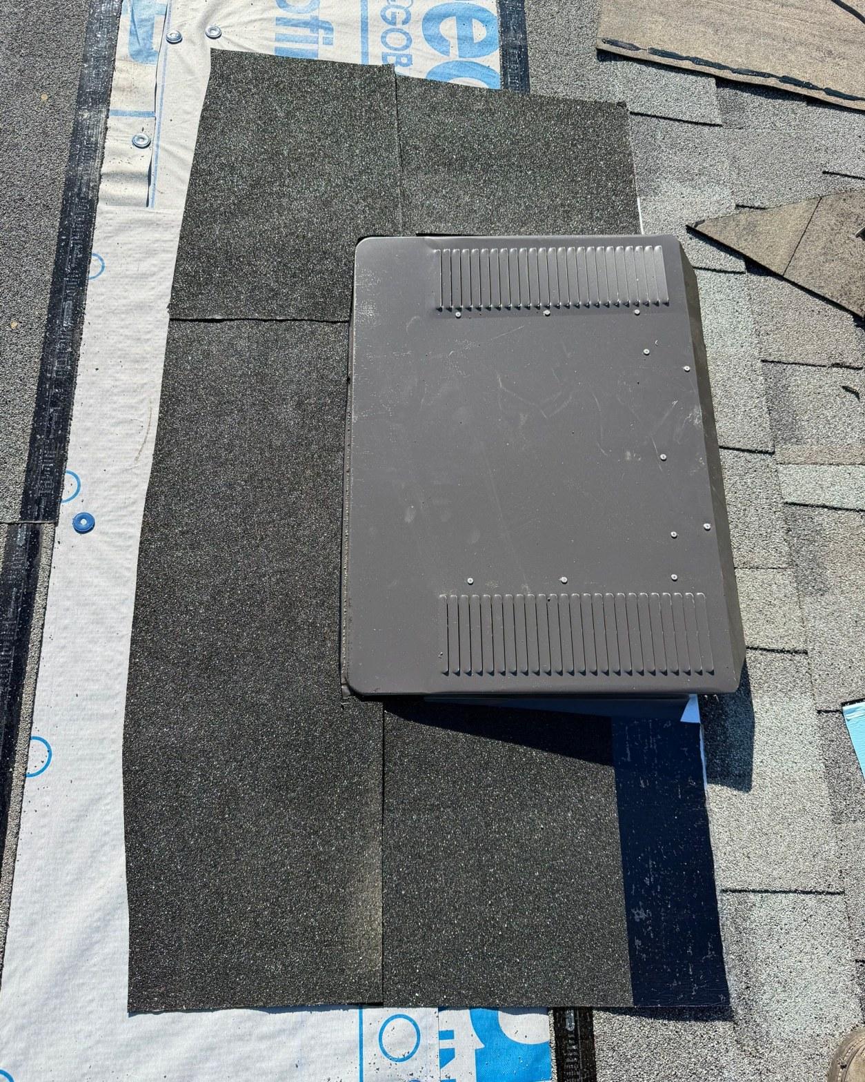 Dark gray plastic roof vent cap on black asphalt shingles with white synthetic underlayment visible during roofing installation.