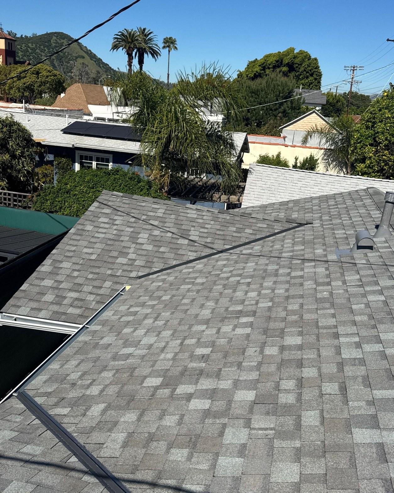 Freshly installed gray architectural asphalt shingles on residential rooftop with vent pipe and skylight visible.