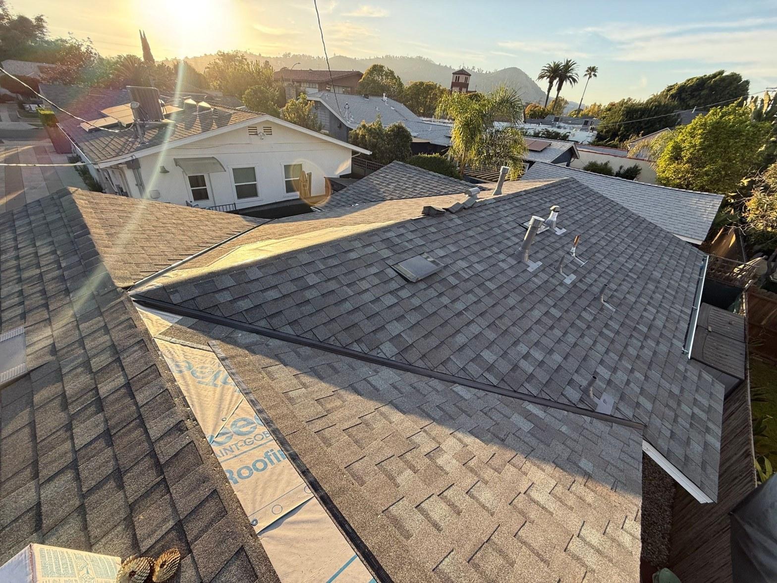 Aerial view of freshly shingled residential roof with Saint-Gobain underlayment visible, vents, and suburban neighborhood background.