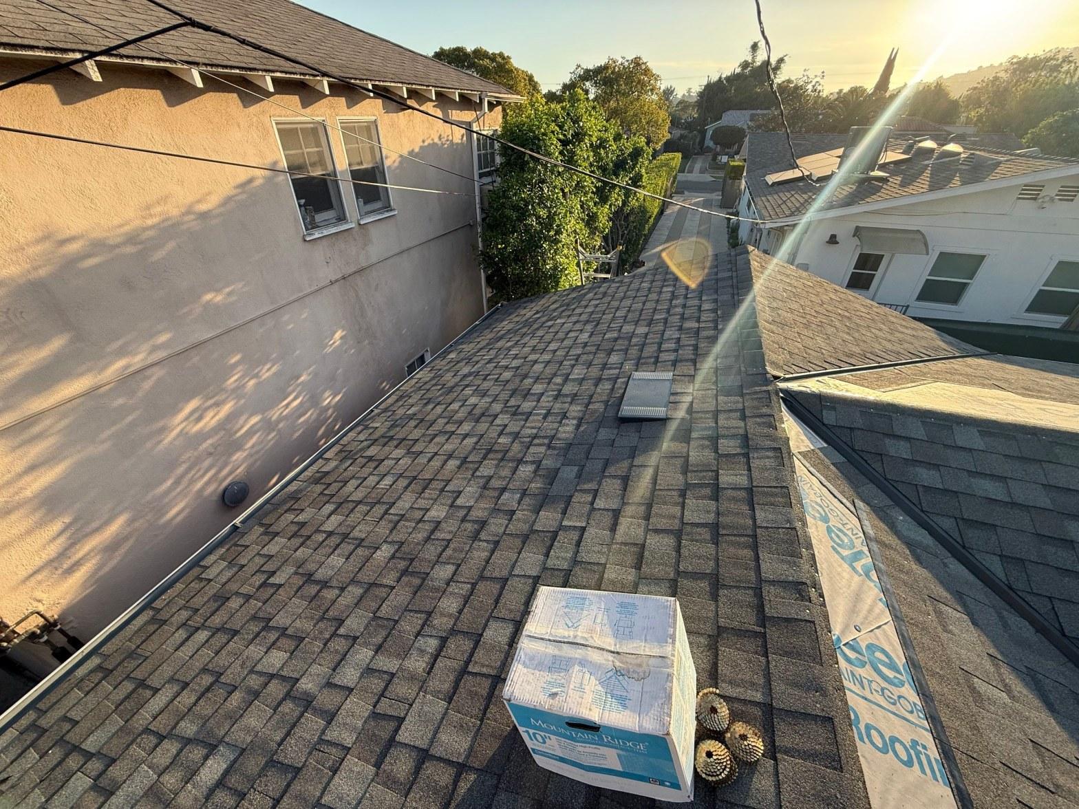 Newly installed gray asphalt shingle roof with Mountain Ridge cap shingle box and coil nails on rooftop.