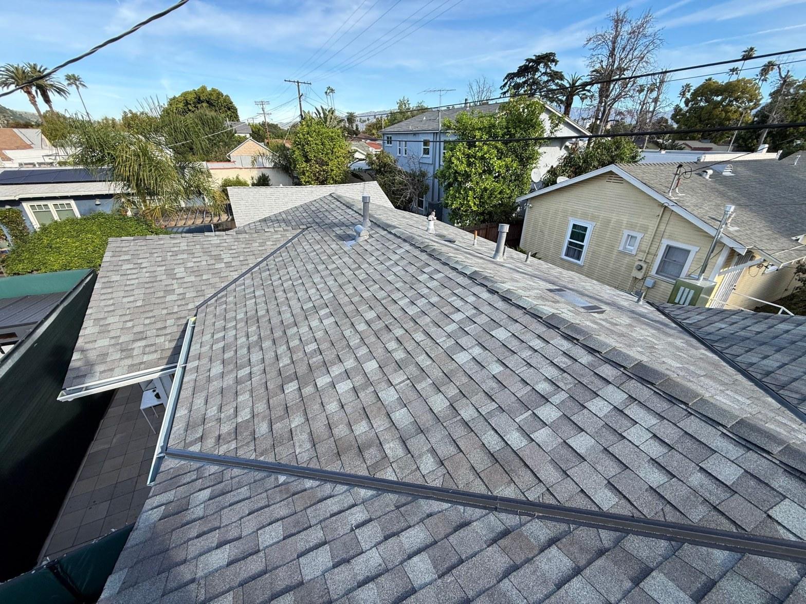 Newly installed gray architectural asphalt shingles on residential roof with plumbing vents and solar panel rails visible.