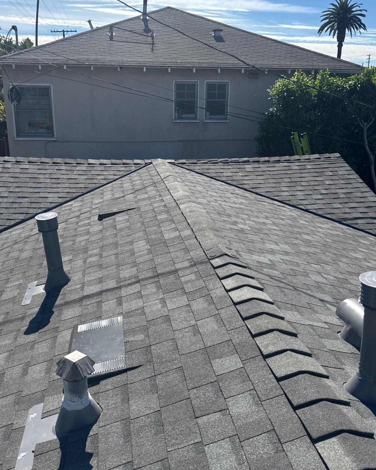 Completed gray asphalt shingle roof with pipe vents, ridge cap, and hip lines on residential home in California.