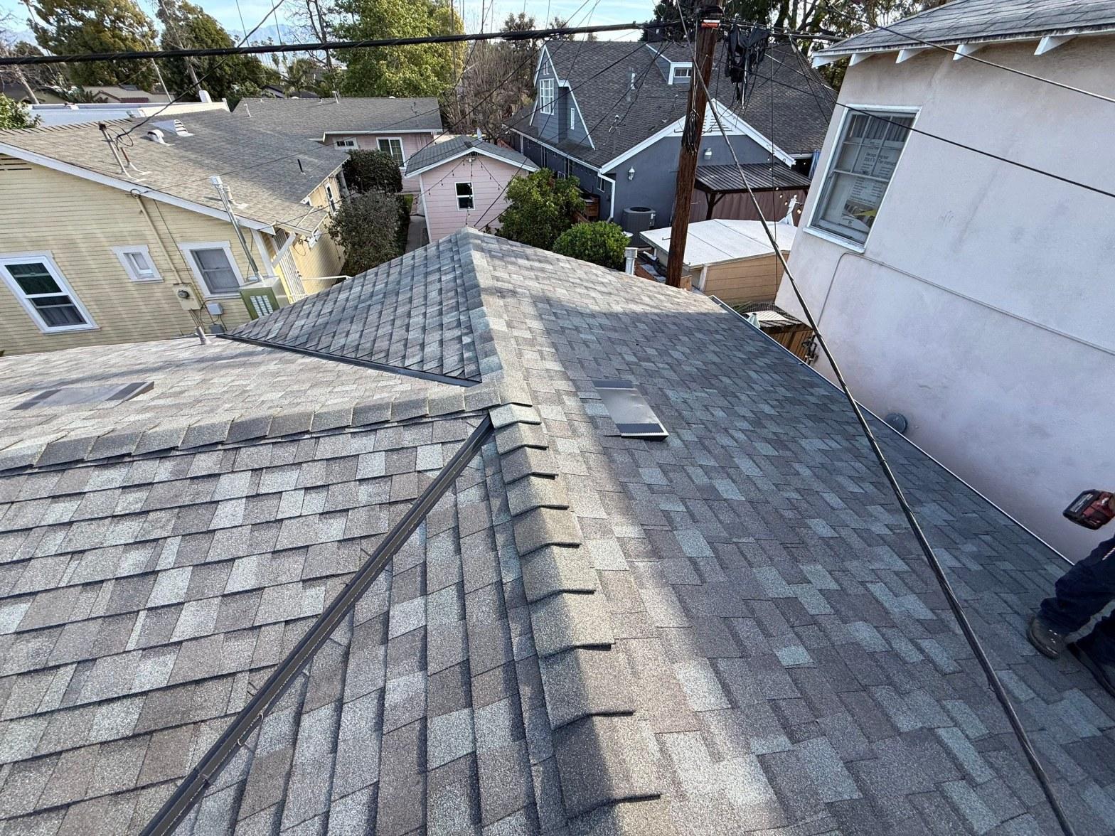 Aerial view of completed gray asphalt shingle roof with hip ridges and valley flashing on residential home.