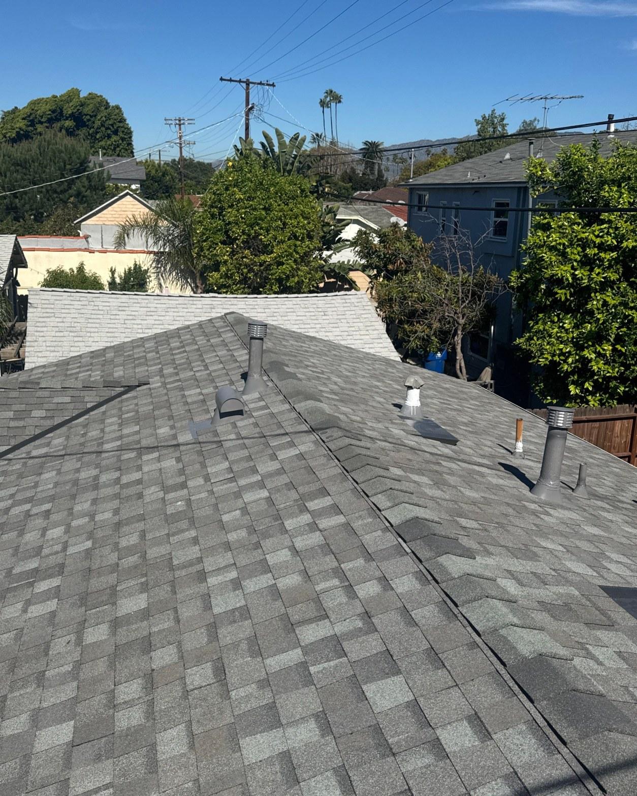 Newly installed gray asphalt shingle roof with pipe vents, ridge lines, and valleys on residential home.