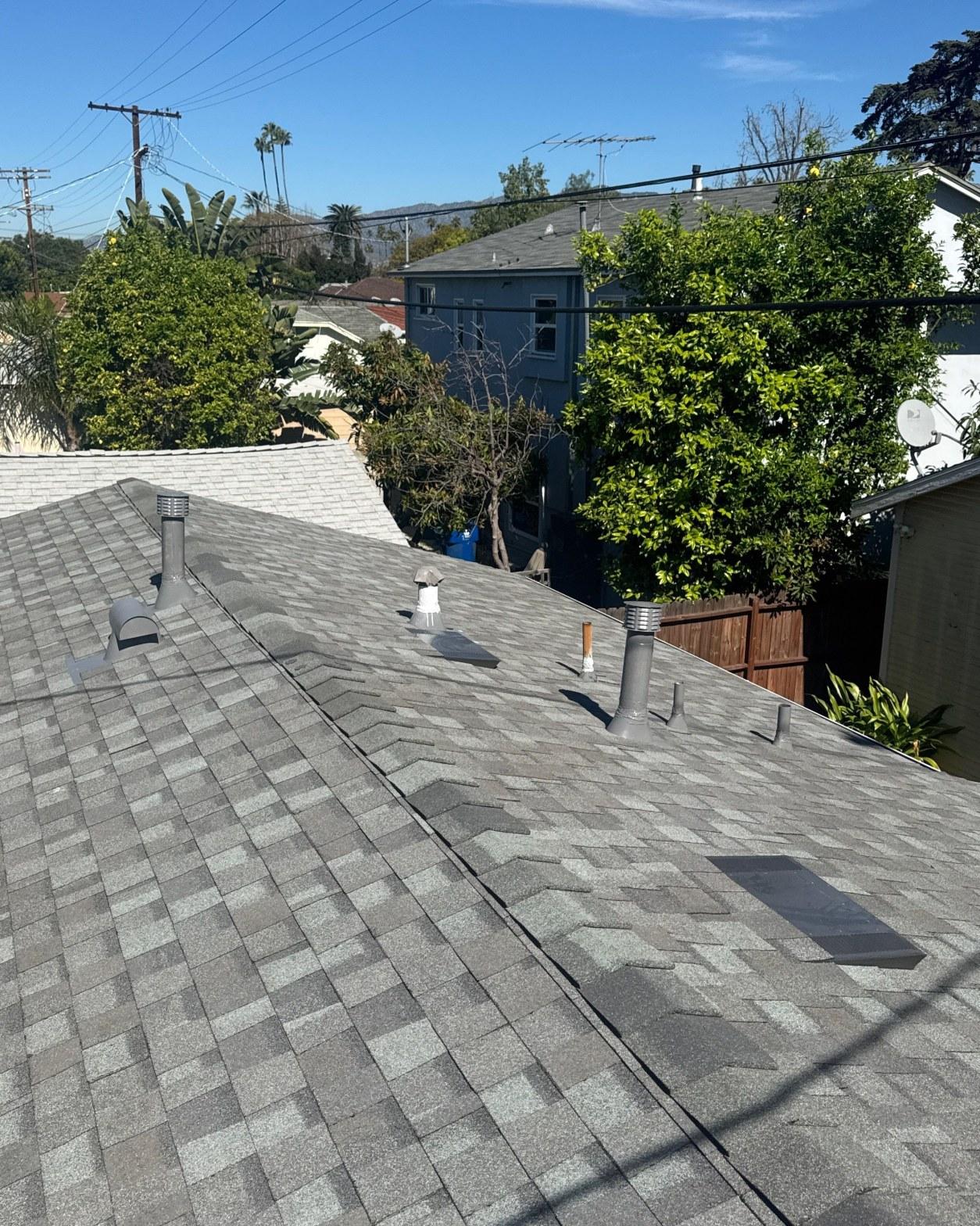 Newly installed gray architectural asphalt shingle roof with plumbing vent pipes on residential home in suburban neighborhood.