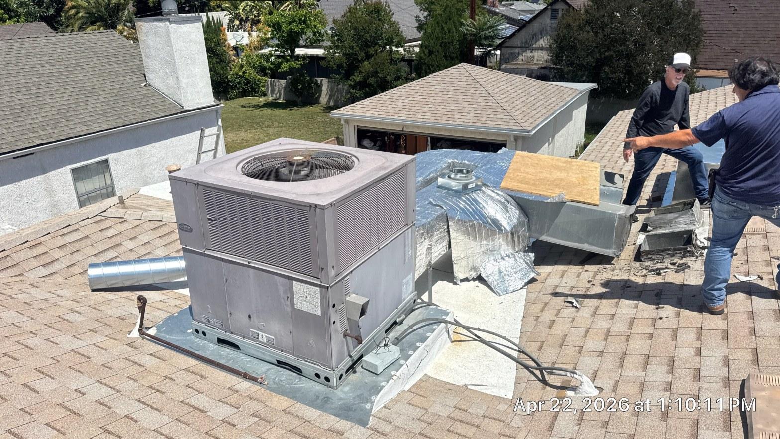 carrier-rooftop-package-unit-installation-burbank-ca-823 Two HVAC technicians on residential roof next to Carrier rooftop package unit with exposed foil ductwork.