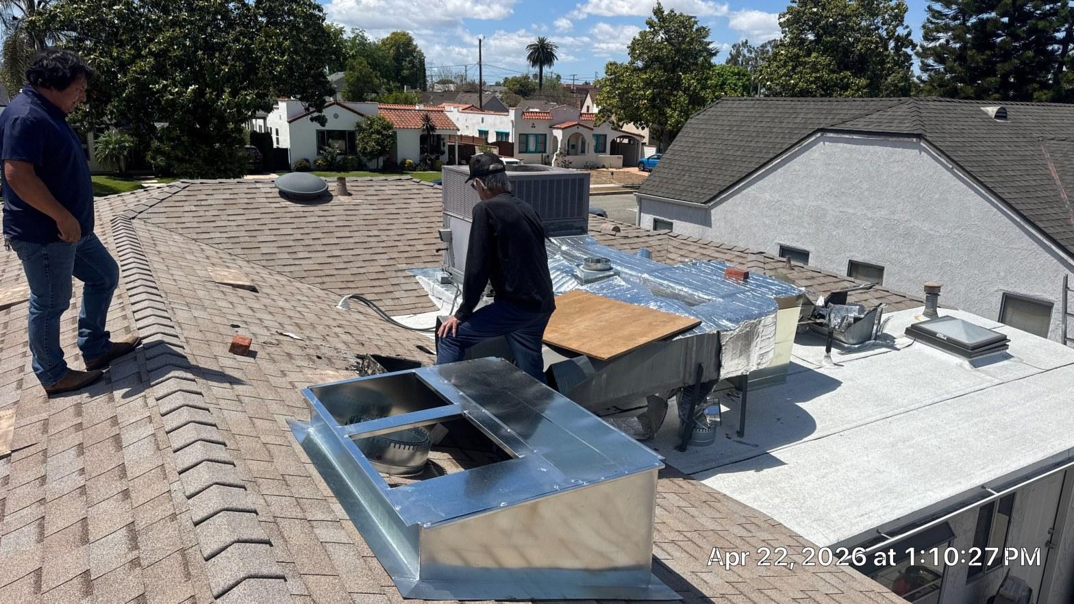 carrier-rooftop-package-unit-installation-burbank-ca-825 Two men on rooftop installing HVAC unit with sheet metal ductwork, insulated plenum, and AC condenser on flat and pitched roof.