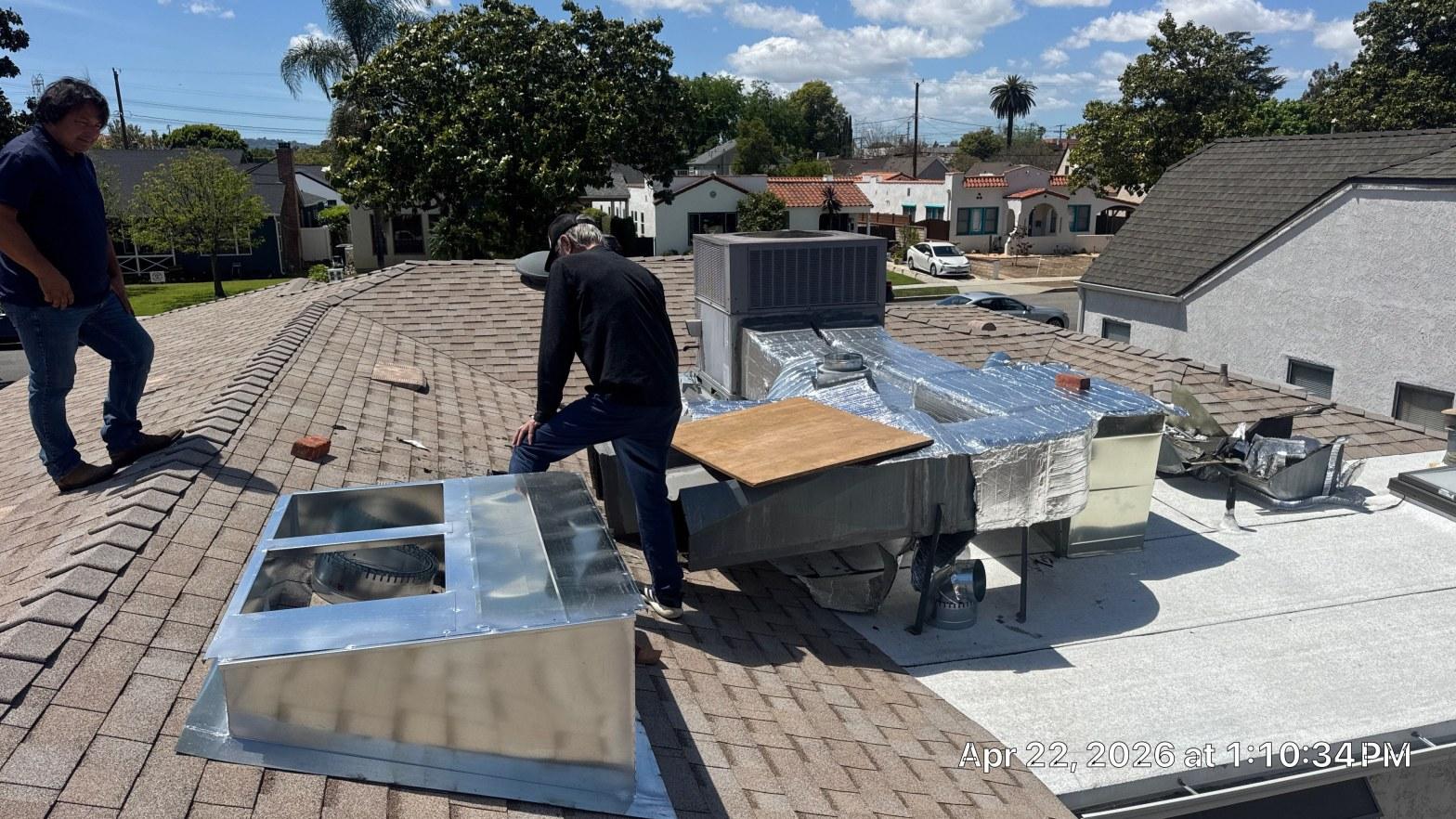 carrier-rooftop-package-unit-installation-burbank-ca-826 Two HVAC technicians on shingle roof installing foil-wrapped ductwork and AC unit with sheet metal plenum box.