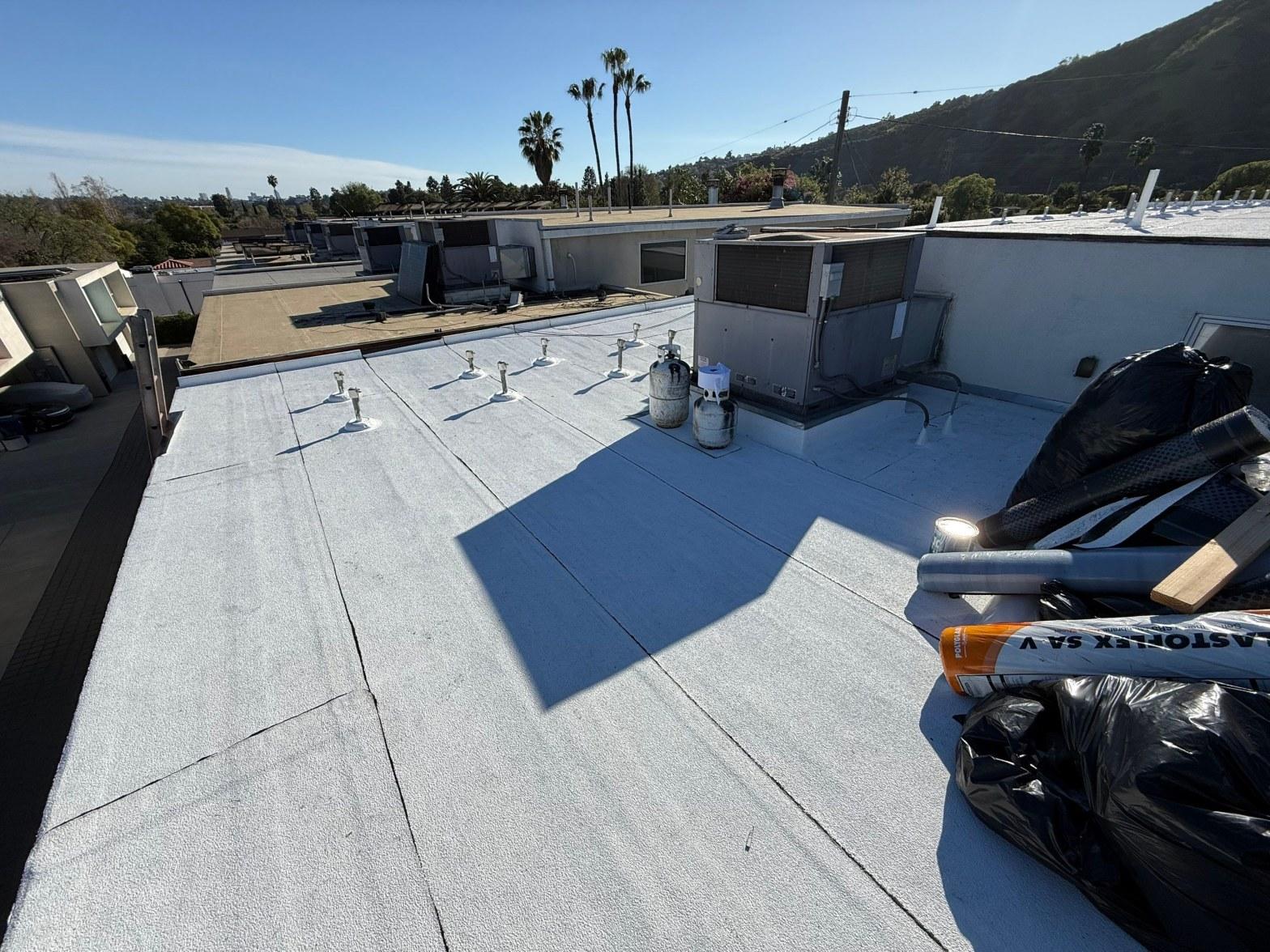 foam-roof-coating-flat-commercial-roof-los-angeles-perlita-a-1000 Flat commercial roof with white modified bitumen membrane, HVAC units, pipe penetrations, and Elastoflex SA V rolls on rooftop.