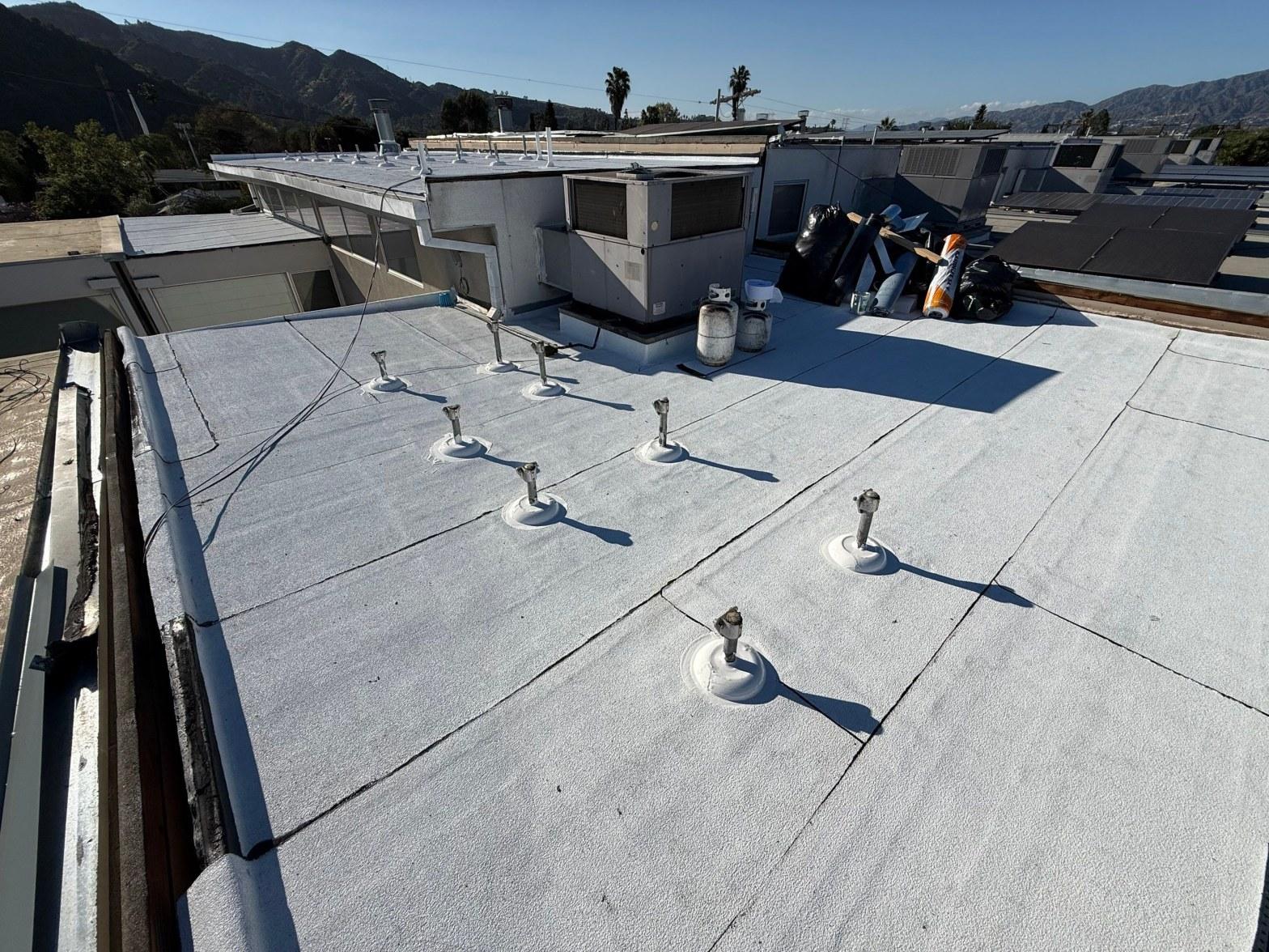 foam-roof-coating-flat-commercial-roof-los-angeles-perlita-a-1002 Freshly coated white flat roof with metal pipe penetration boots, HVAC units, and mountains in background.
