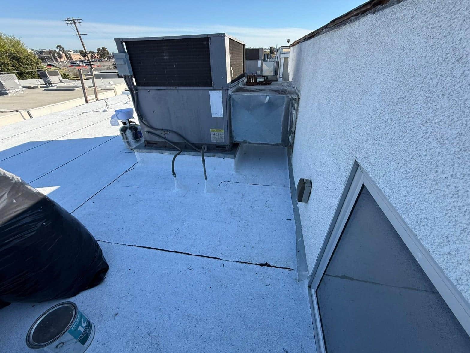 foam-roof-coating-flat-commercial-roof-los-angeles-perlita-a-1004 Commercial flat roof showing visible cracks in white elastomeric coating beside rooftop HVAC package units and stucco parapet wall.