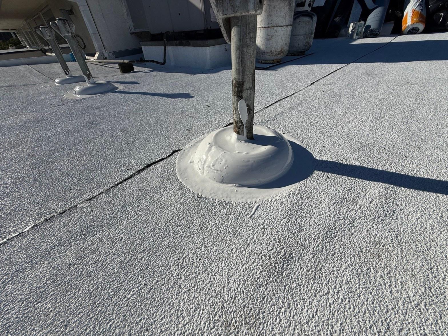 foam-roof-coating-flat-commercial-roof-los-angeles-perlita-a-1008 White elastomeric sealant mound around metal pipe penetration on a flat commercial roof with visible seams.
