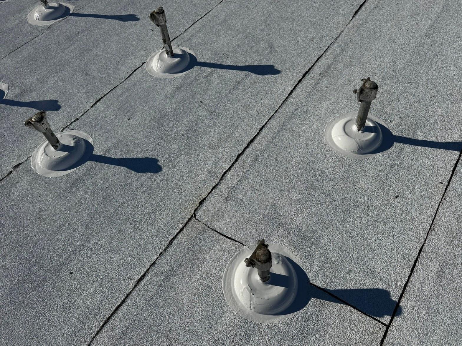 foam-roof-coating-flat-commercial-roof-los-angeles-perlita-a-1010 Close-up of metal roof fasteners with white dome plates on a flat gray TPO or foam roofing membrane.