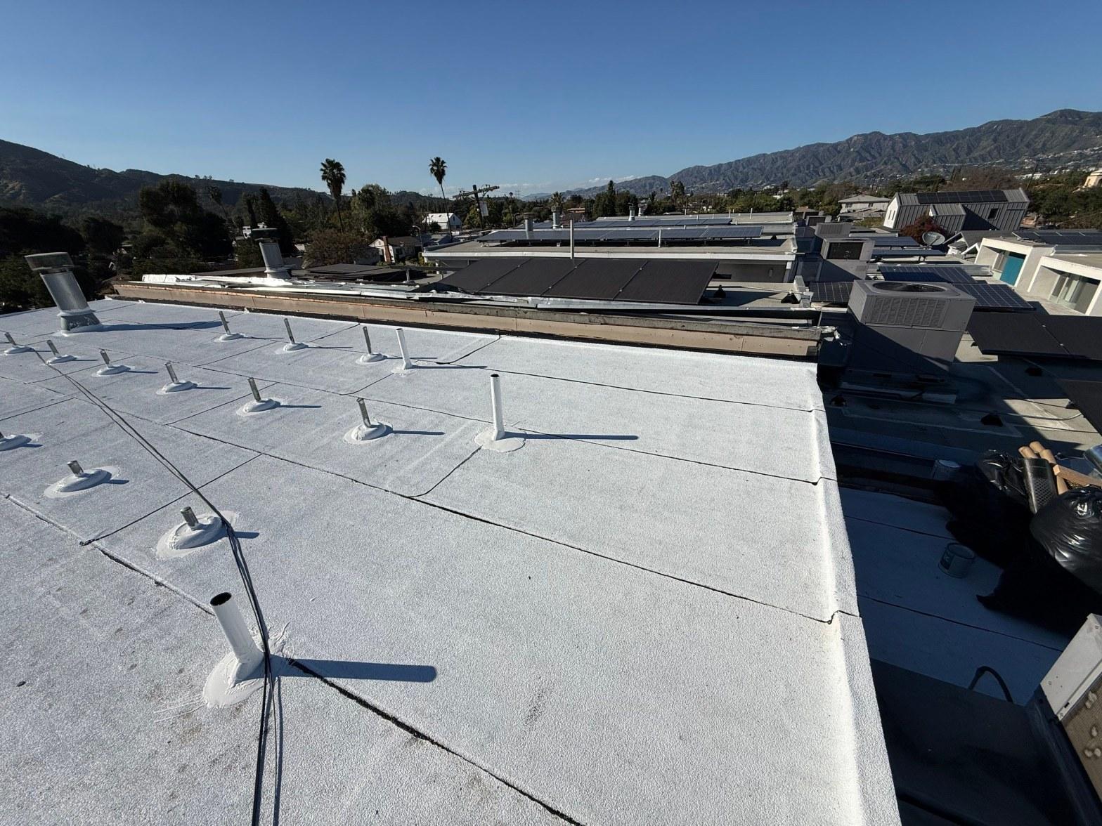 White spray foam flat roof with multiple pipe penetrations, mountains and solar panels visible in background, Los Angeles area.