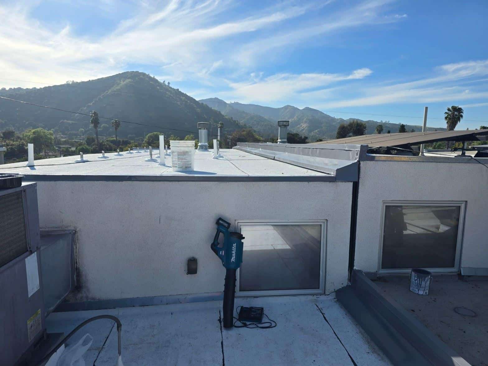 foam-roof-coating-flat-commercial-roof-los-angeles-perlita-a-983 Makita cordless tool on white flat roof with vents, skylights, and green mountains in background.
