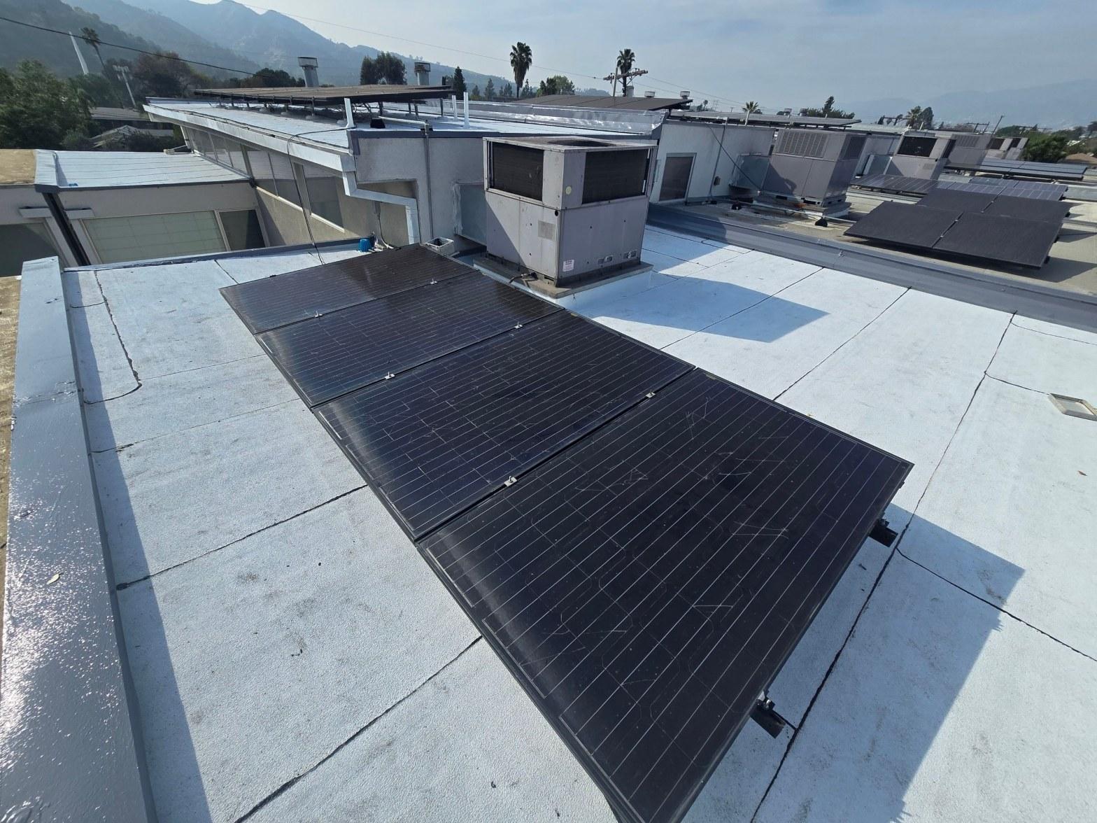 foam-roof-coating-flat-commercial-roof-los-angeles-perlita-a-984 Black monocrystalline solar panels mounted on flat white commercial roof with rooftop HVAC units and mountains in background.