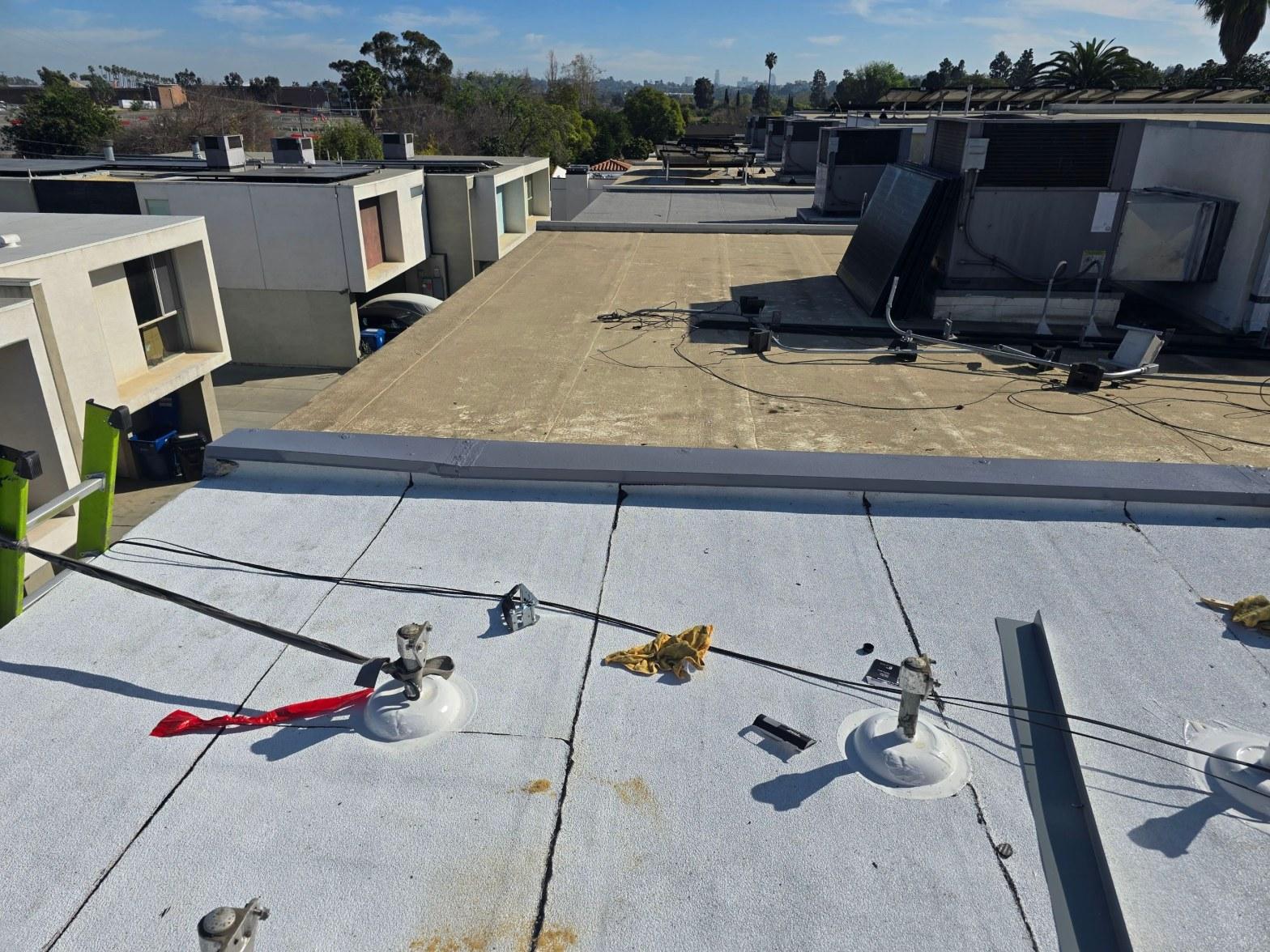 foam-roof-coating-flat-commercial-roof-los-angeles-perlita-a-985 Commercial flat roof showing satellite antenna mounts, loose cables, HVAC equipment, and adjoining rooftops in urban setting.