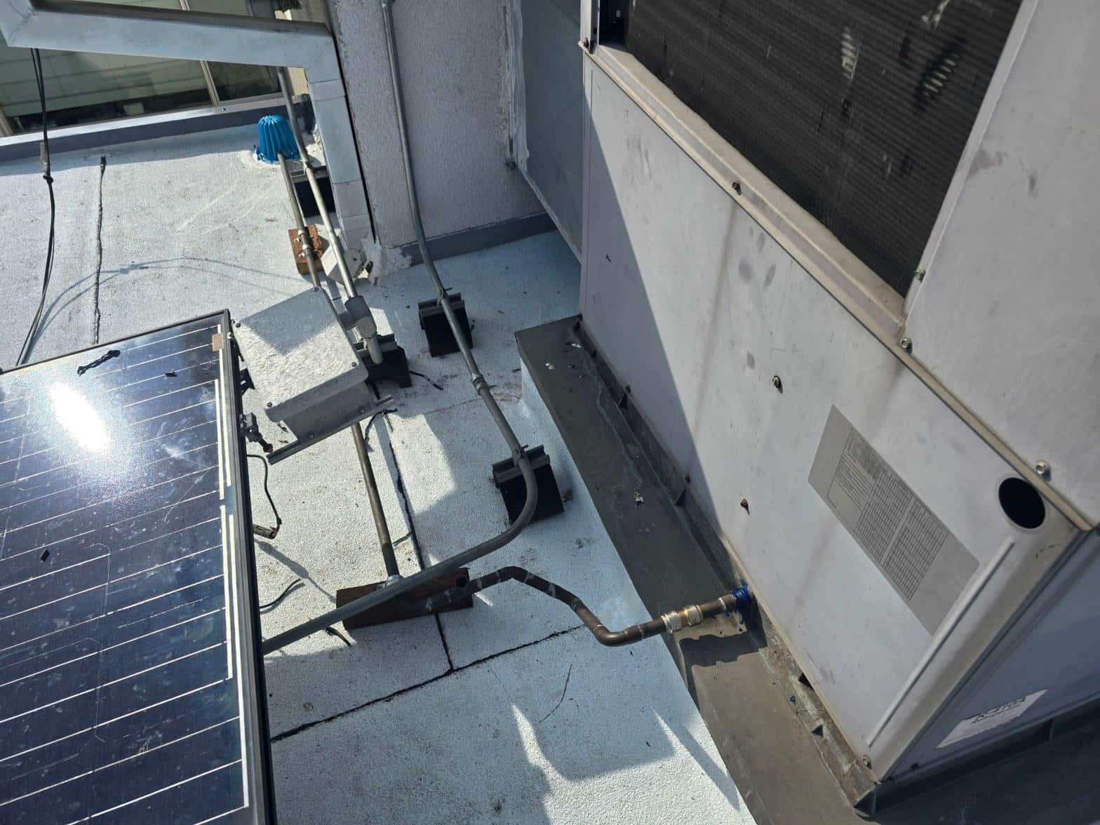 foam-roof-coating-flat-commercial-roof-los-angeles-perlita-a-987 Rooftop solar panel beside commercial HVAC unit with copper refrigerant lines and piping connections on flat roof.