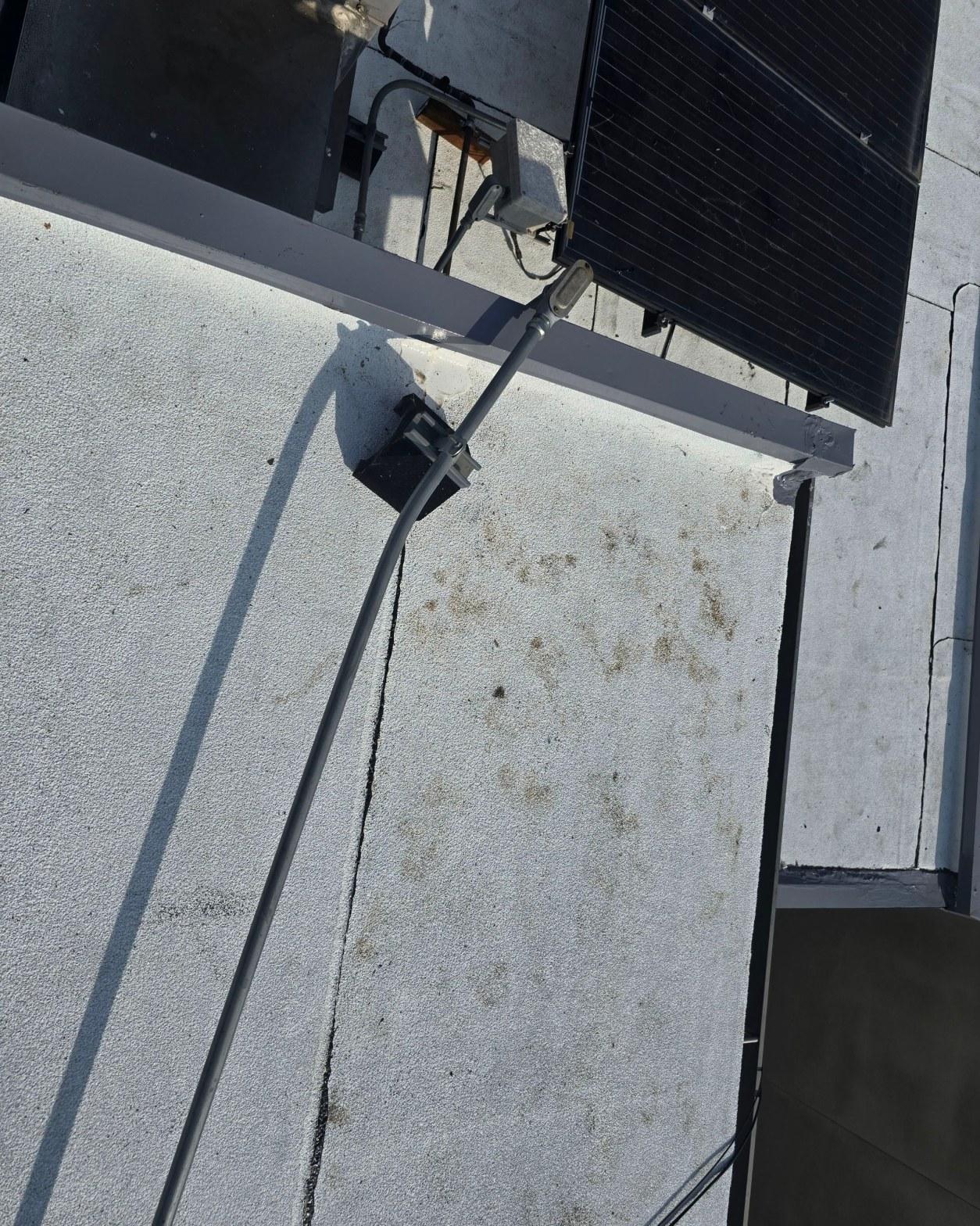 foam-roof-coating-flat-commercial-roof-los-angeles-perlita-a-989 Solar panel wiring and gray conduit running down white stucco exterior wall from rooftop solar array.