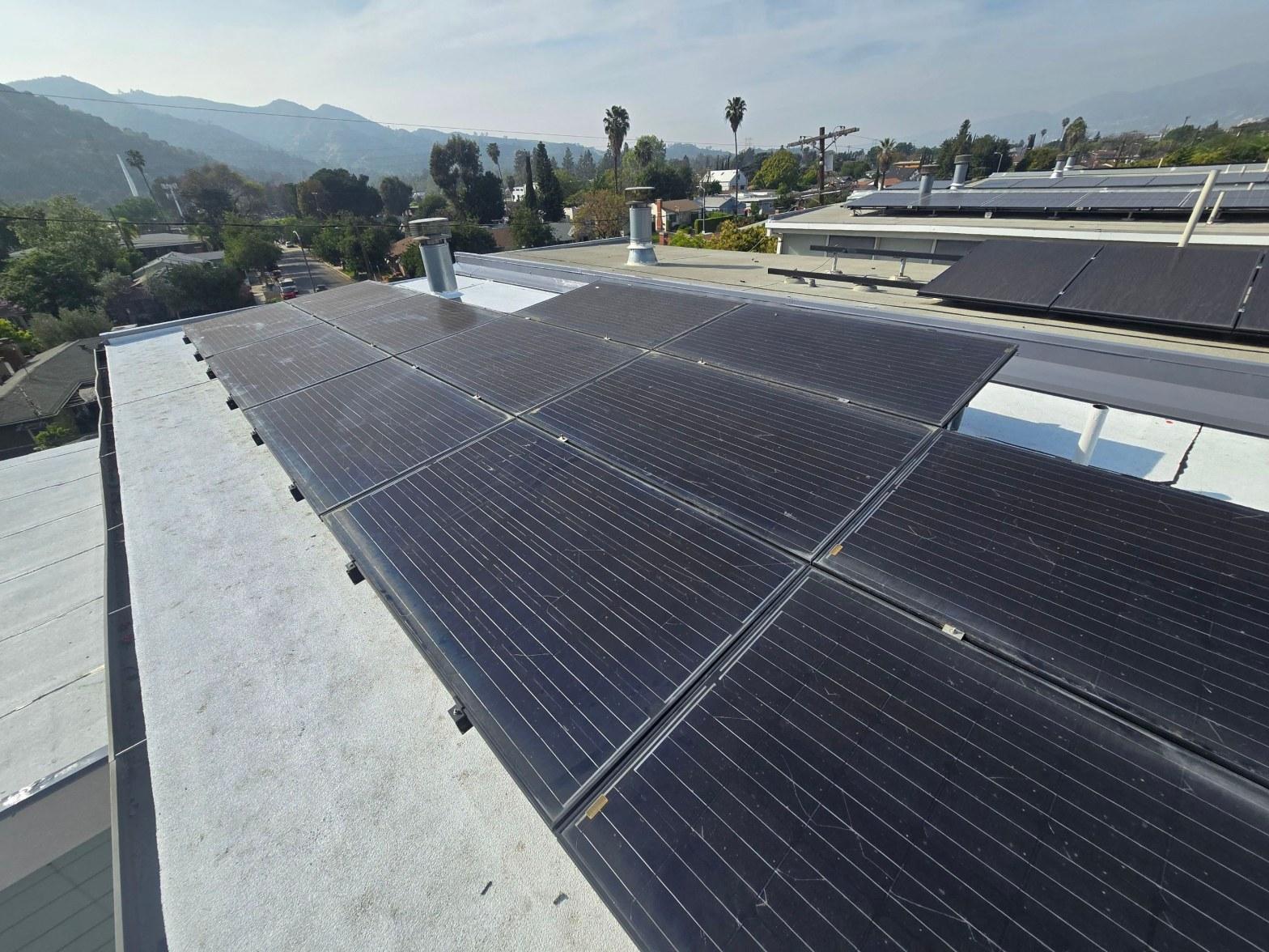 foam-roof-coating-flat-commercial-roof-los-angeles-perlita-a-990 Black solar panels mounted on flat white residential roof in Los Angeles with mountains and palm trees in background.