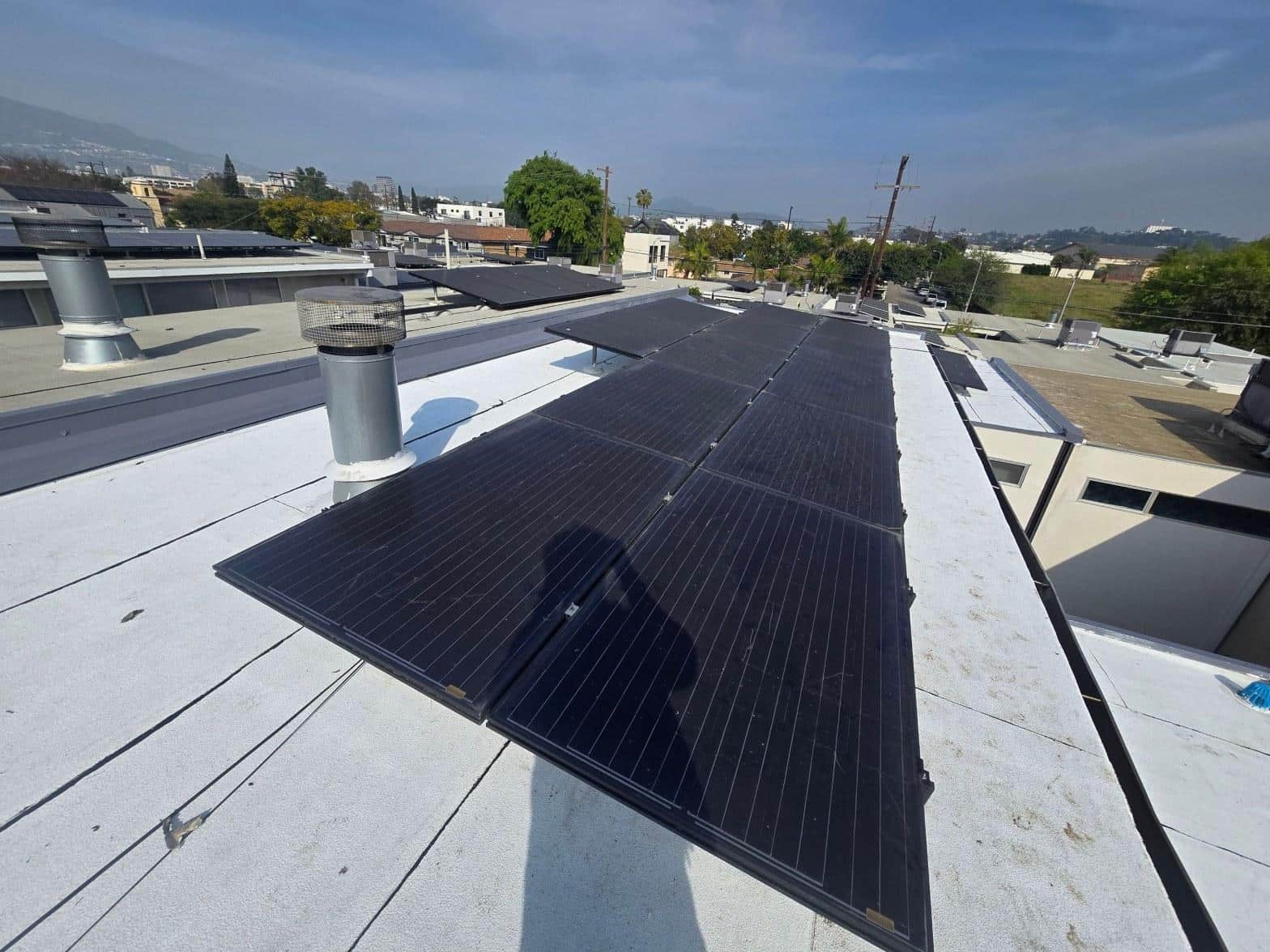 foam-roof-coating-flat-commercial-roof-los-angeles-perlita-a-991 Black monocrystalline solar panels mounted on flat white commercial roof with urban neighborhood visible in background.