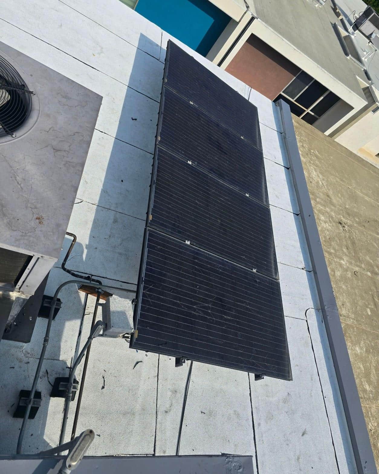 foam-roof-coating-flat-commercial-roof-los-angeles-perlita-a-992 Four black monocrystalline solar panels installed on flat white commercial rooftop with HVAC unit nearby.