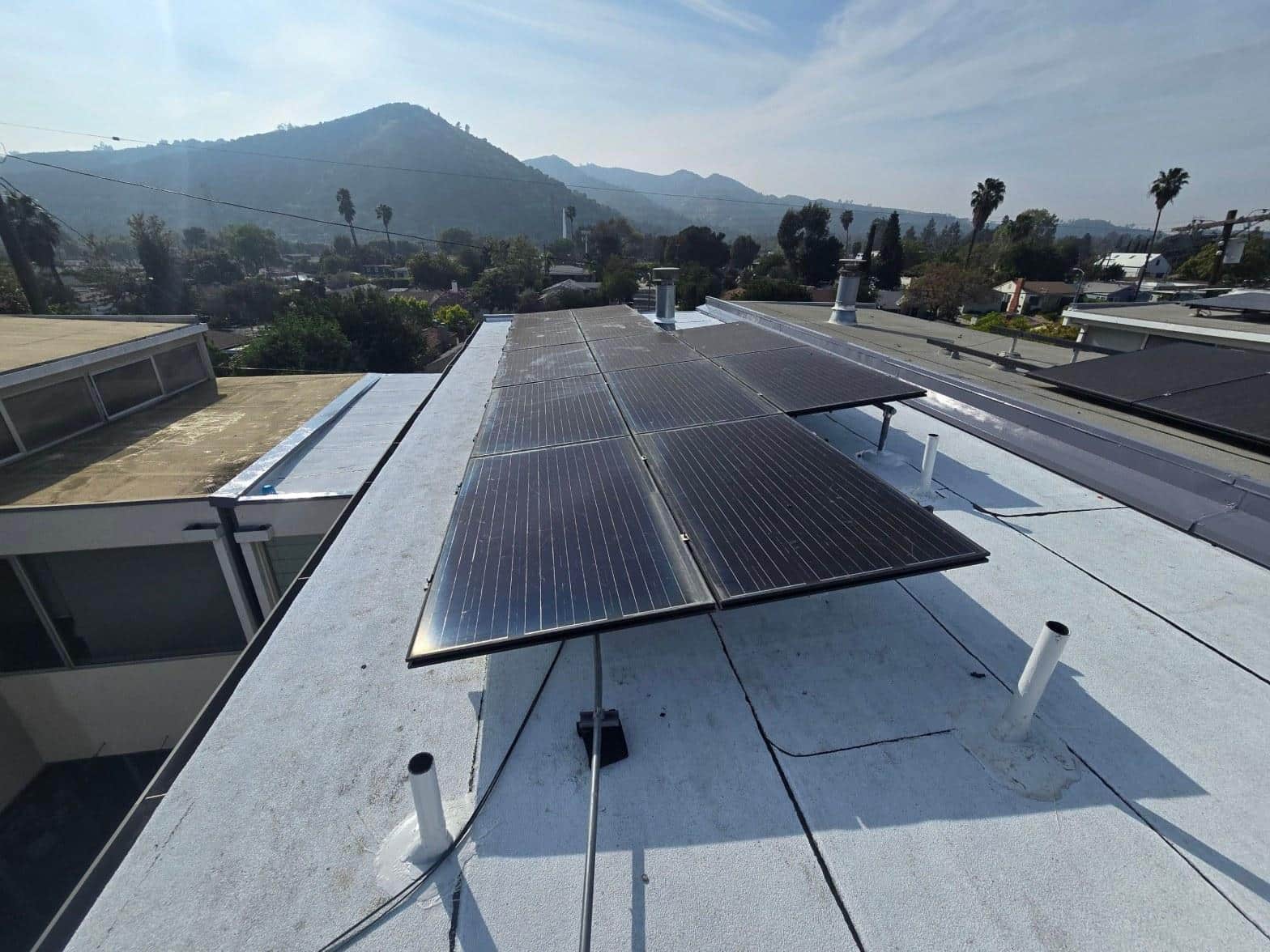 foam-roof-coating-flat-commercial-roof-los-angeles-perlita-a-993 Eight black solar panels mounted on flat white residential roof in Los Angeles with hills in background.