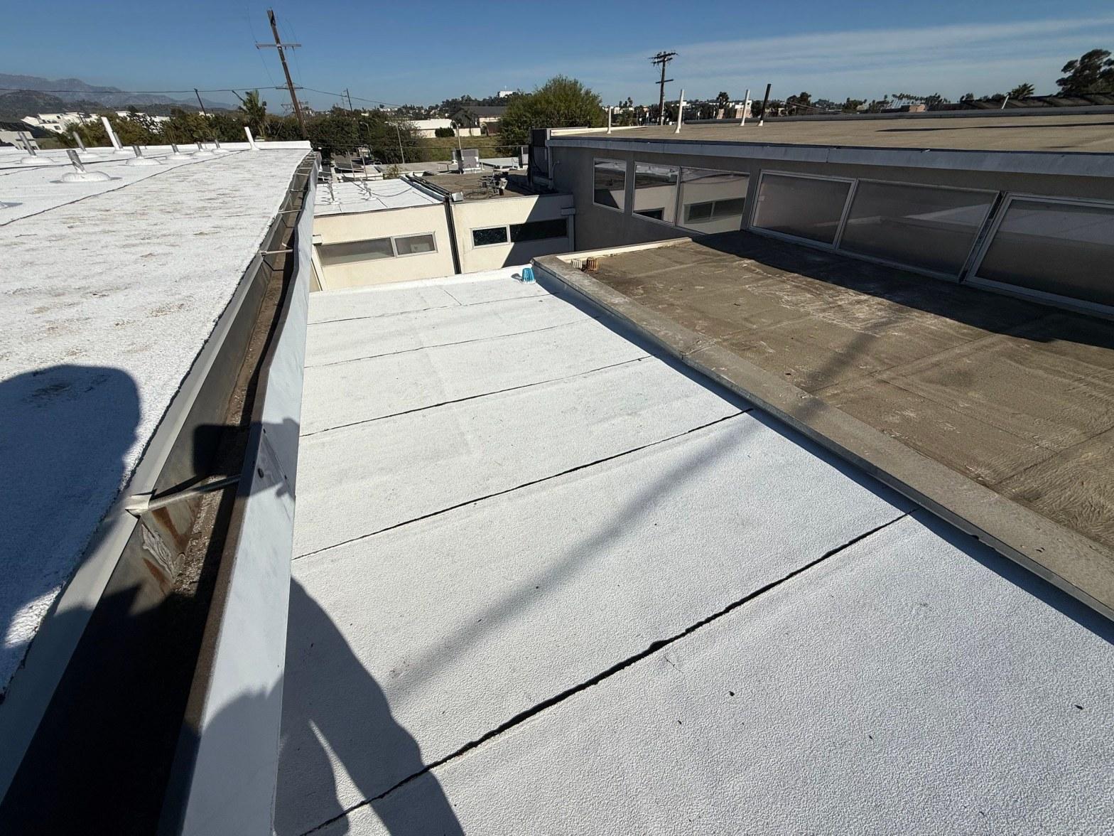foam-roof-coating-flat-commercial-roof-los-angeles-perlita-a-999 White elastomeric coating on commercial flat roof with metal drip edge, panel seams, and adjacent rooftop sections visible.