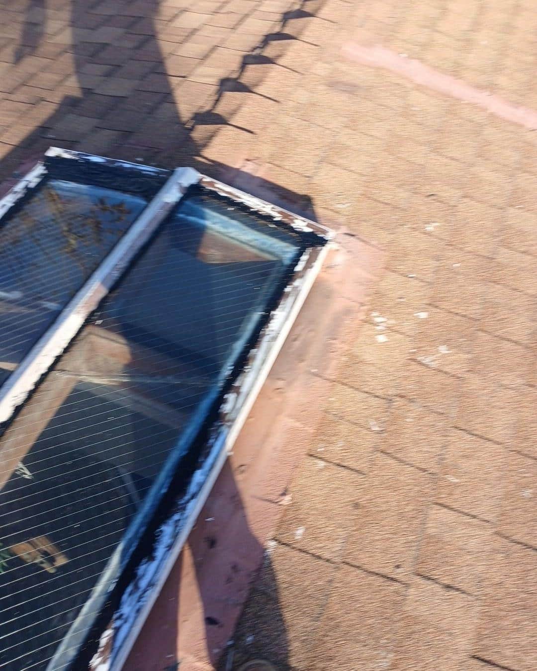 Close-up of cracked skylight frame with peeling sealant on worn asphalt shingle roof, showing water damage risk.