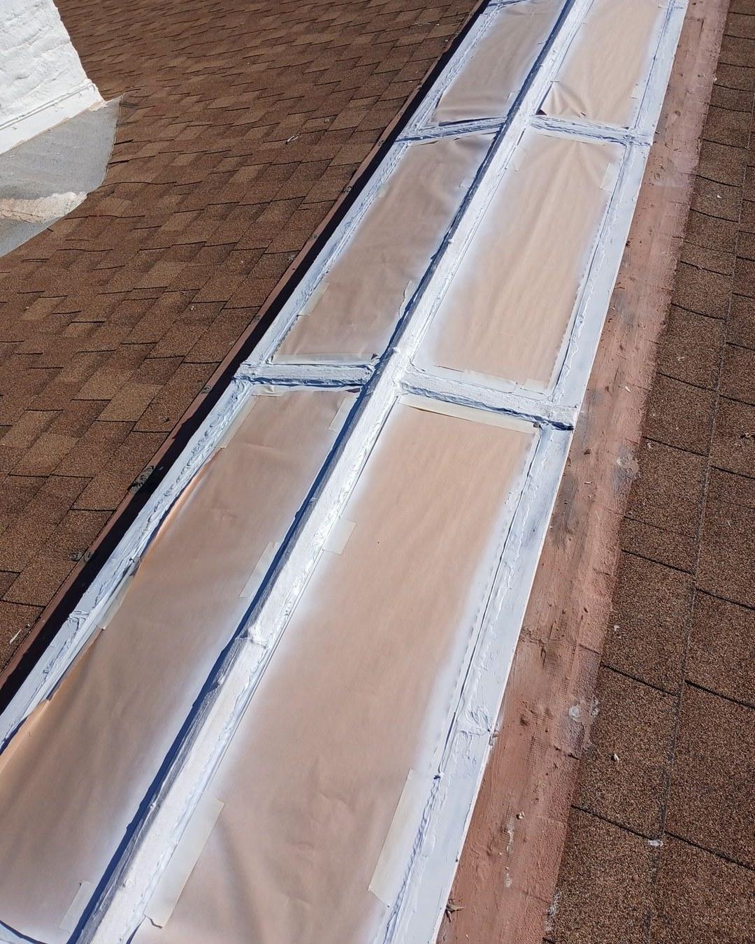 Row of roof skylights with white caulk seals and protective film on brown asphalt shingle roof.