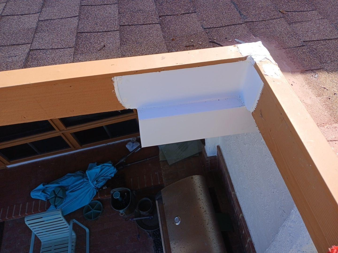 Roof corner with fascia board removed showing open eave gap, asphalt shingles above and patio below.