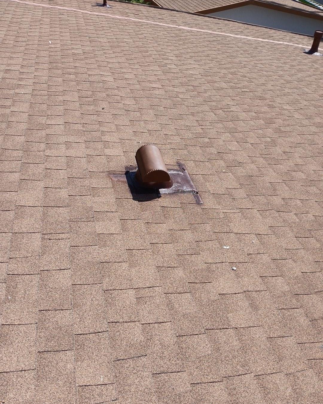 Brown metal pipe boot flashing on tan asphalt shingle roof with lead collar seal around vent pipe.