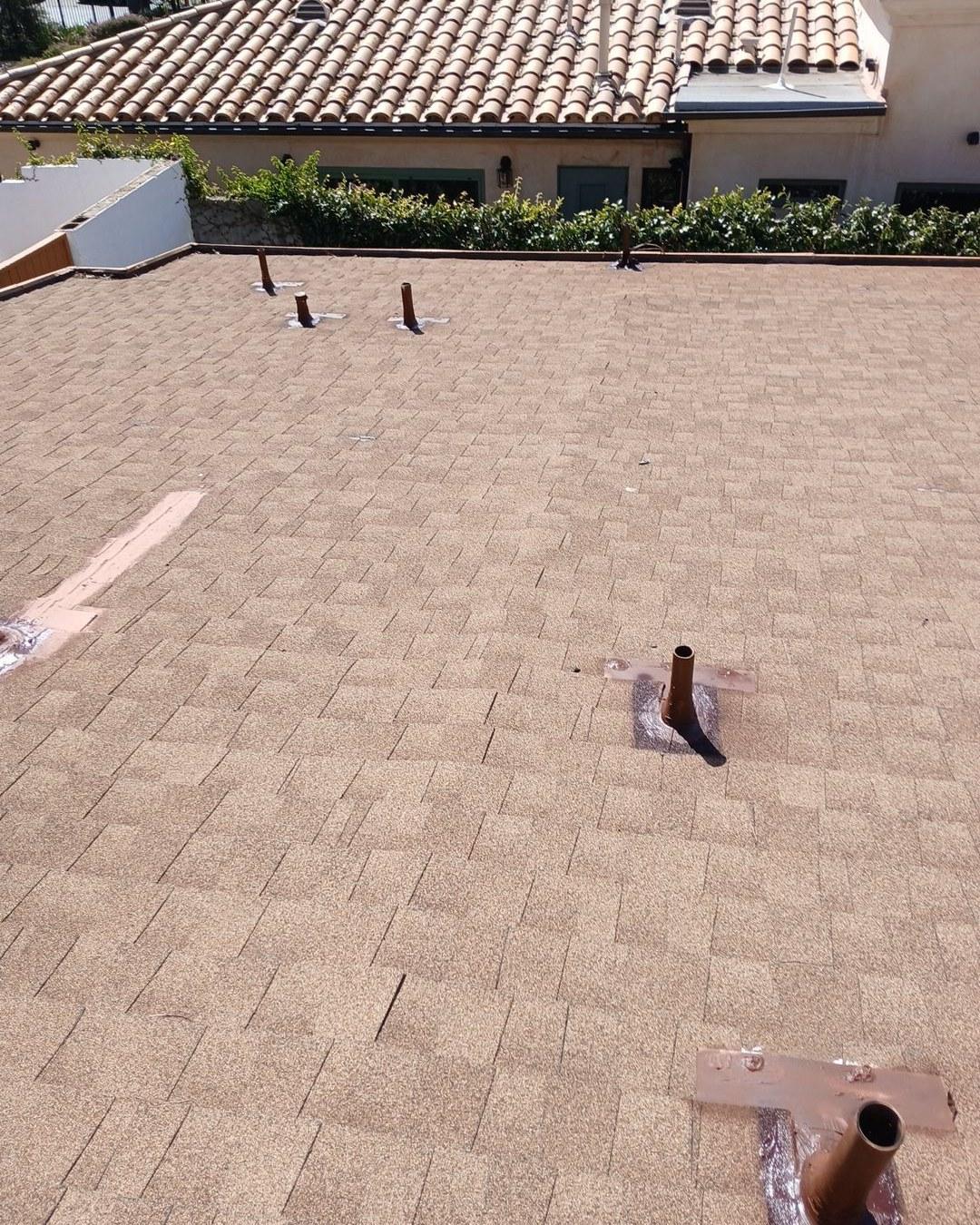 Freshly installed tan asphalt shingle roof with multiple pipe boot penetrations and metal flashing on residential home.