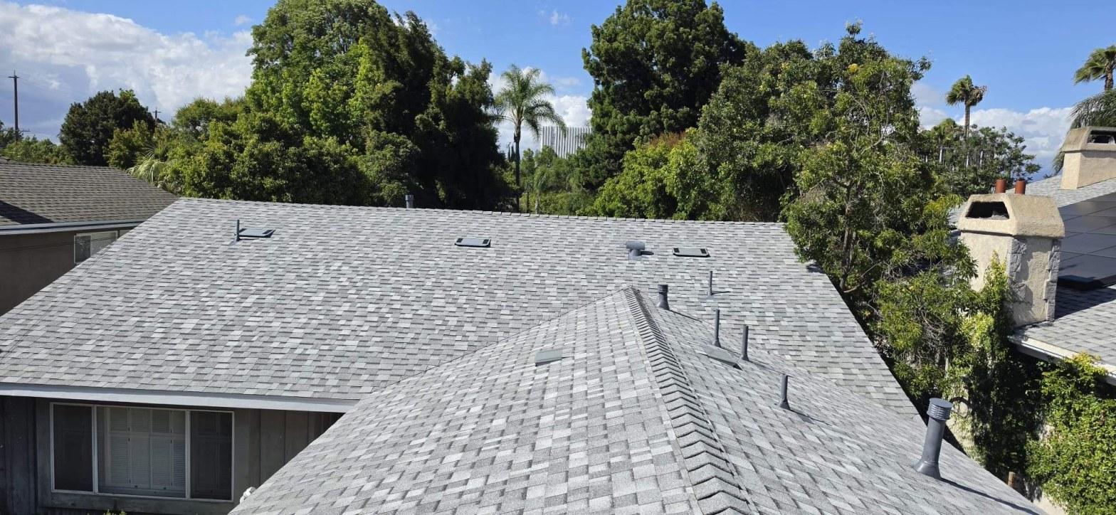 Aerial view of new gray architectural asphalt shingle roof with pipe vents and skylights on single-story home.