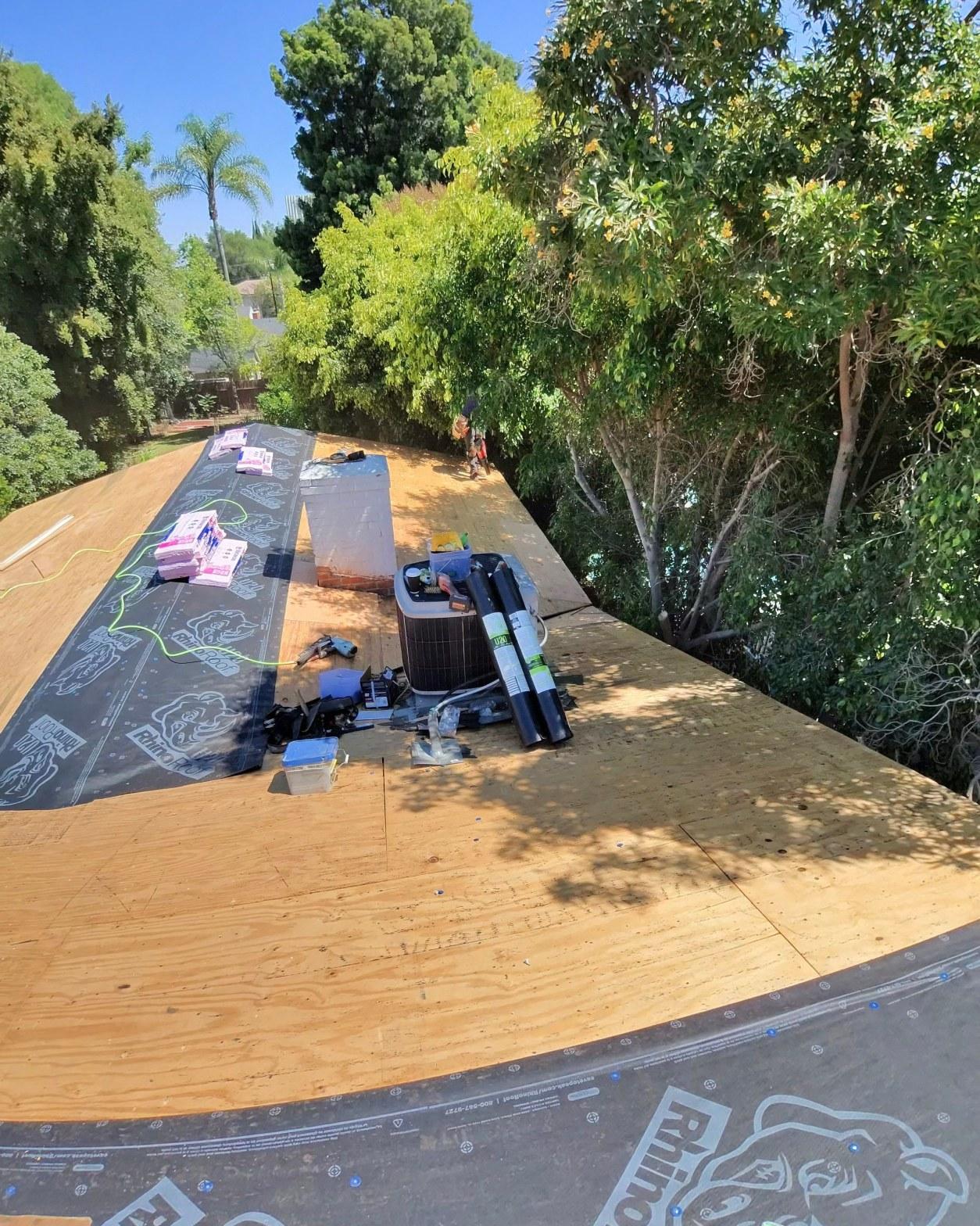 shingle-reroof-14819-sutton-st-los-angeles-560 Roof replacement in progress showing plywood decking, Rhino synthetic underlayment rolls, and HVAC condenser unit on residential roof.