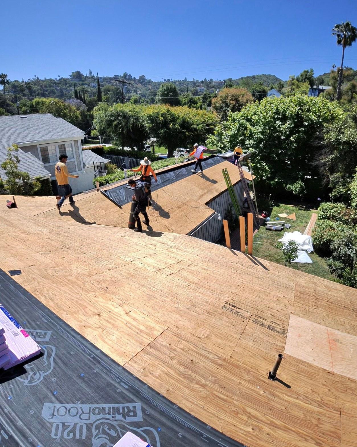 shingle-reroof-14819-sutton-st-los-angeles-561 Four roofers rolling out RhinoRoof U20 underlayment over new plywood sheathing on steep residential roof.