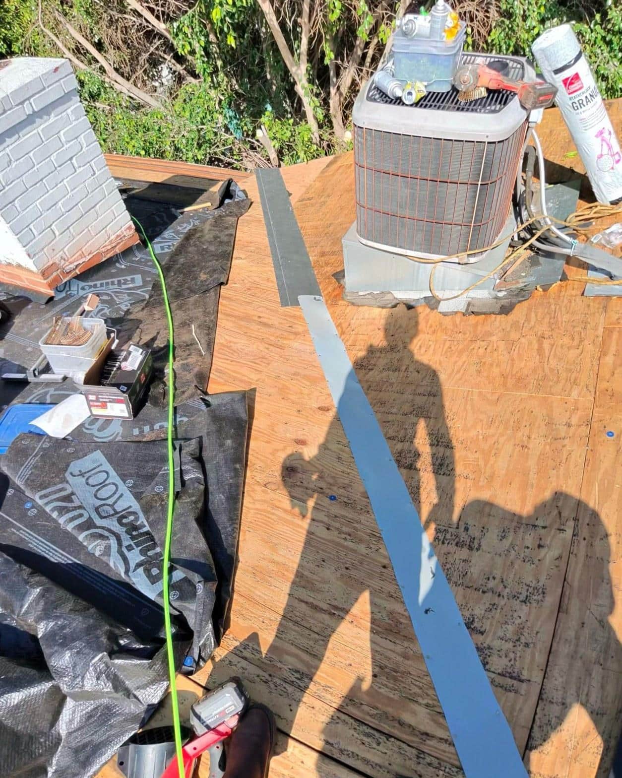 shingle-reroof-14819-sutton-st-los-angeles-564 Plywood roof deck exposed during re-roofing project with HVAC condenser unit, metal drip edge, and roofing underlayment materials.