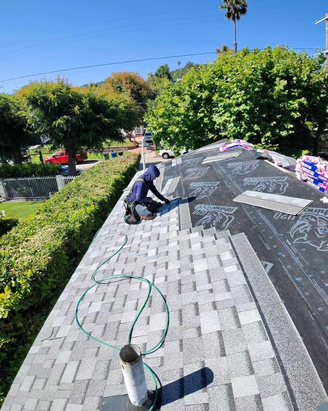 shingle-reroof-14819-sutton-st-los-angeles-567 Roofer kneeling on partially shingled roof installing gray asphalt shingles over RhinoRoof synthetic underlayment.