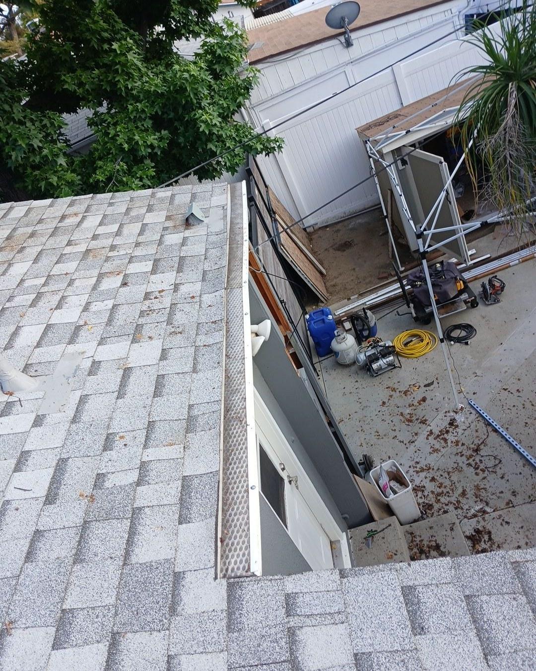 shingle-reroof-6643-saloma-ave-los-angeles-662 Perforated white gutter guard on asphalt shingle roof edge overlooking concrete yard with scaffolding and tools.