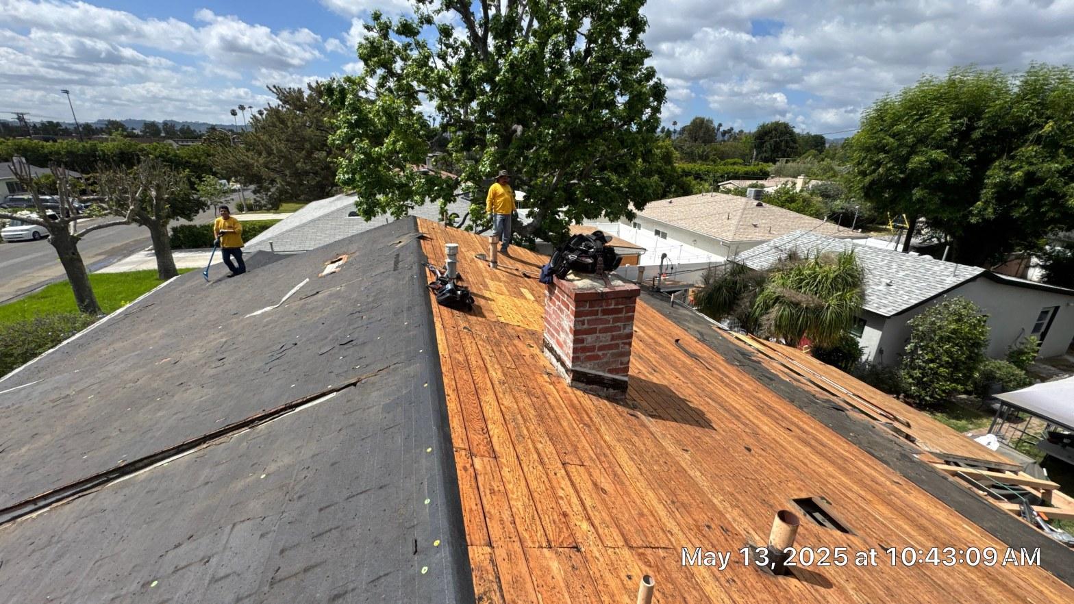 shingle-reroof-6643-saloma-ave-los-angeles-667 Two roofers in yellow shirts removing old shingles, exposing wood decking and brick chimney on residential home.