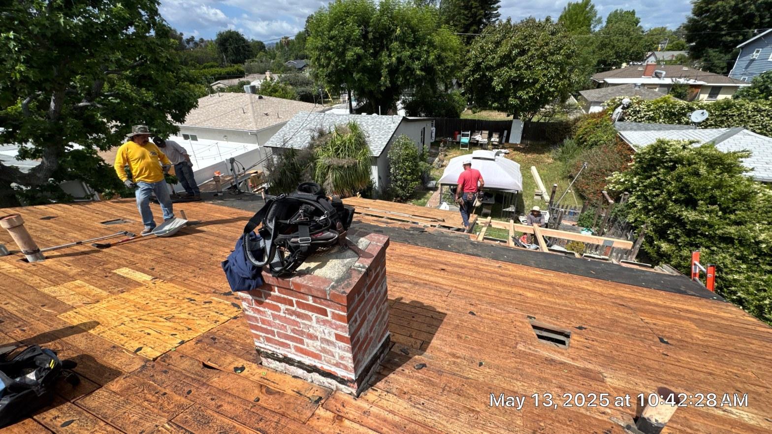 shingle-reroof-6643-saloma-ave-los-angeles-668 Roofers removing old roofing material exposing wood sheathing on residential home with brick chimney in foreground.