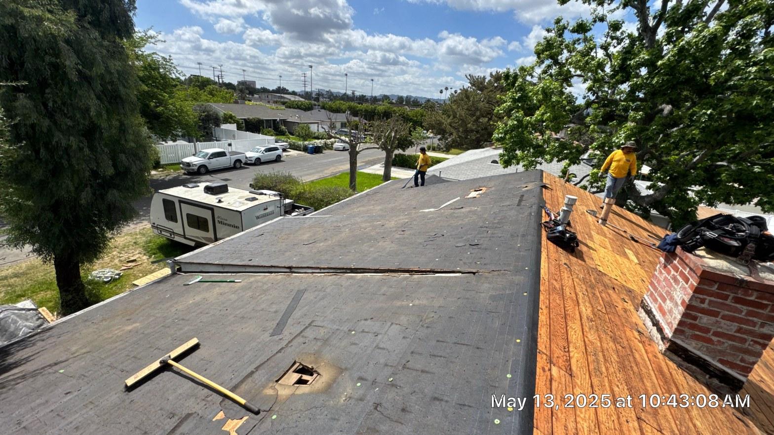 shingle-reroof-6643-saloma-ave-los-angeles-669 Two roofers in yellow shirts removing old asphalt shingles from residential roof, exposing plywood decking and brick chimney.