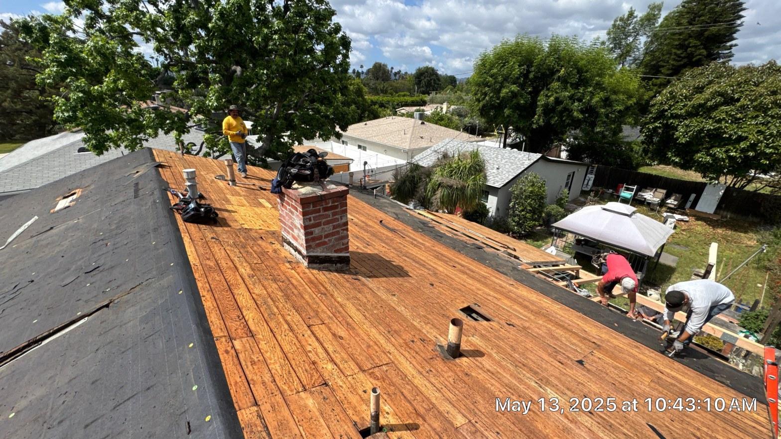 shingle-reroof-6643-saloma-ave-los-angeles-670 Roofing crew removing shingles and installing underlayment on wood plank roof deck with brick chimney, May 2025.