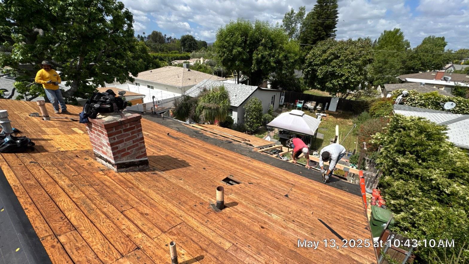 shingle-reroof-6643-saloma-ave-los-angeles-671 Roof tear-off in progress showing exposed wood sheathing, brick chimney, and three workers on residential home.
