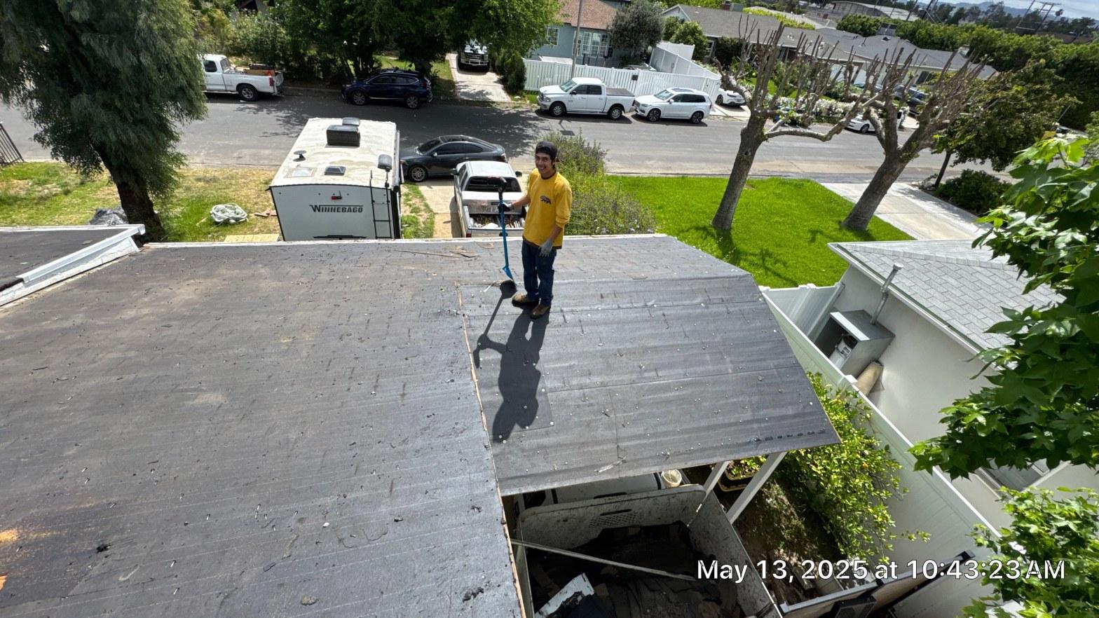 shingle-reroof-6643-saloma-ave-los-angeles-672 Man in yellow shirt using pry bar to tear off flat roof membrane, suburban neighborhood background, May 2025.