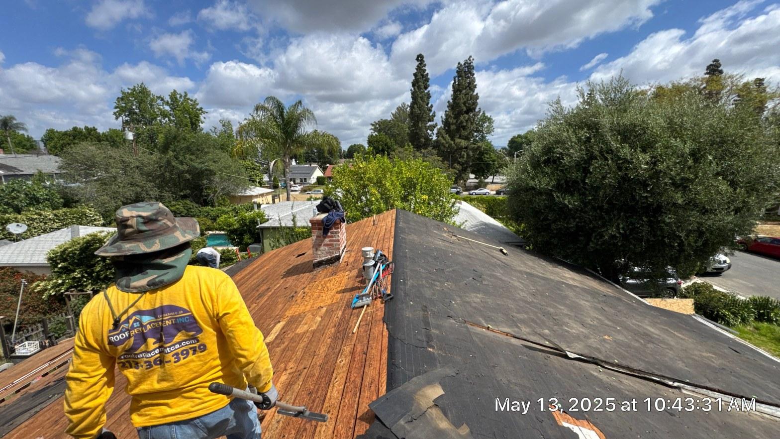 shingle-reroof-6643-saloma-ave-los-angeles-674 Roofing contractor in yellow Roof Replacement Inc. shirt removing asphalt shingles, exposing wood decking on residential roof.